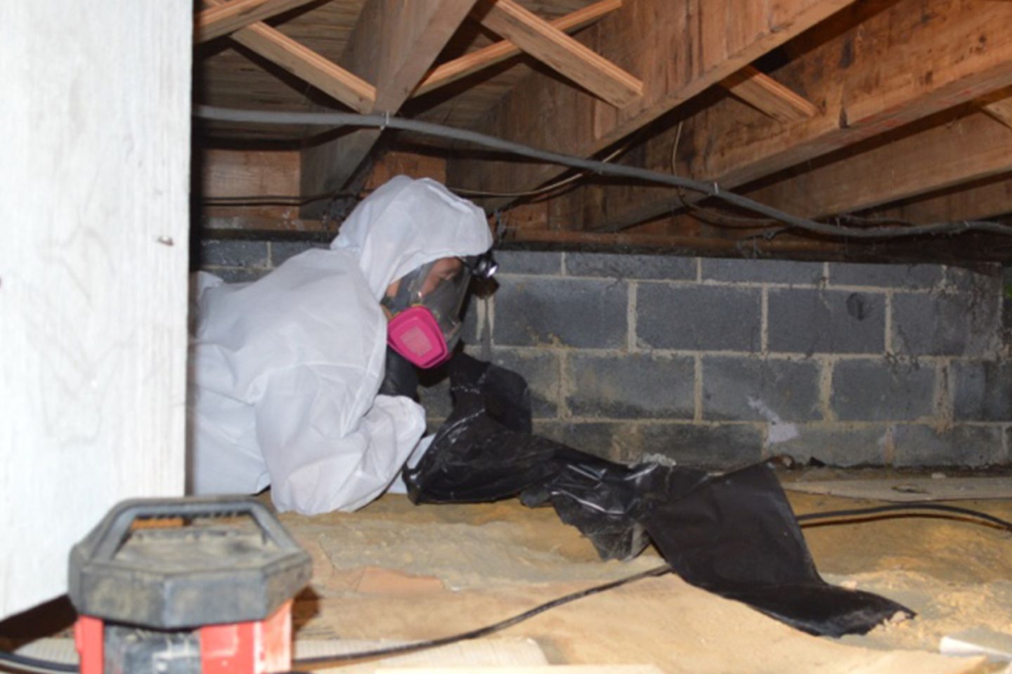 A man wearing a white suit and mask works on mold removal in a basement crawl space in Rockford, IL.