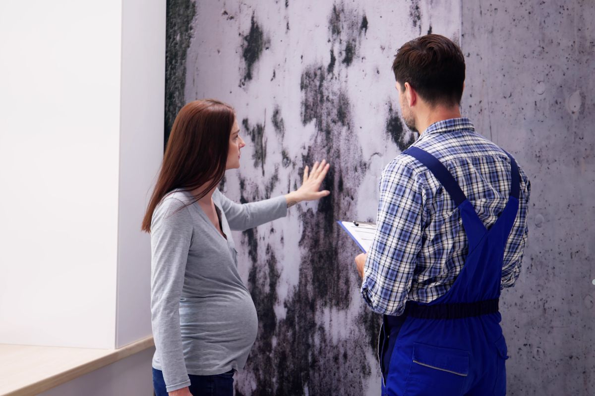 A man and woman stand before a moldy wall, highlighting the health risks associated with mold exposure.