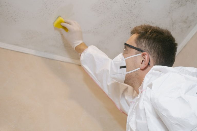 A man wearing protective gear and a white coat is removing mold from a ceiling, promoting cleanliness and safety.